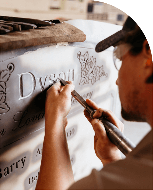 A man is carving a name on a wall with a tool.