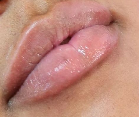 Close-up of a person's slightly parted lips, appearing moist and light pink, with a hint of gloss.