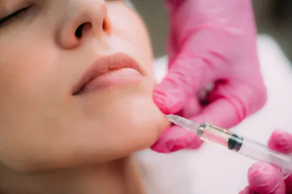 Close-up of a person receiving a facial injection from a gloved hand with a syringe