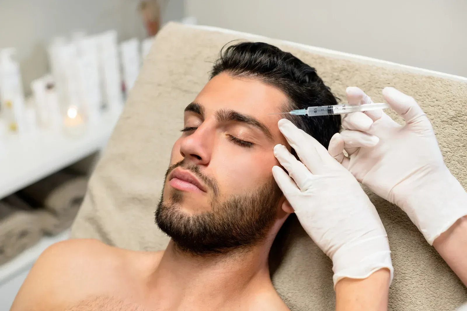 Man receiving injection near his eyebrow at a medical spa, wearing gloves and lying down.