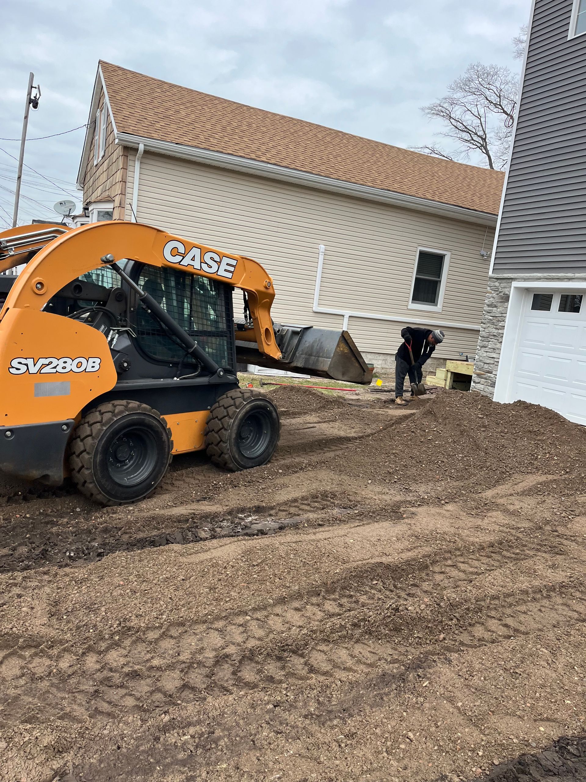 Masonry company near Shrewsbury NJ. Orange CASE skid steer moving dirt beside a white house on a muddy construction site