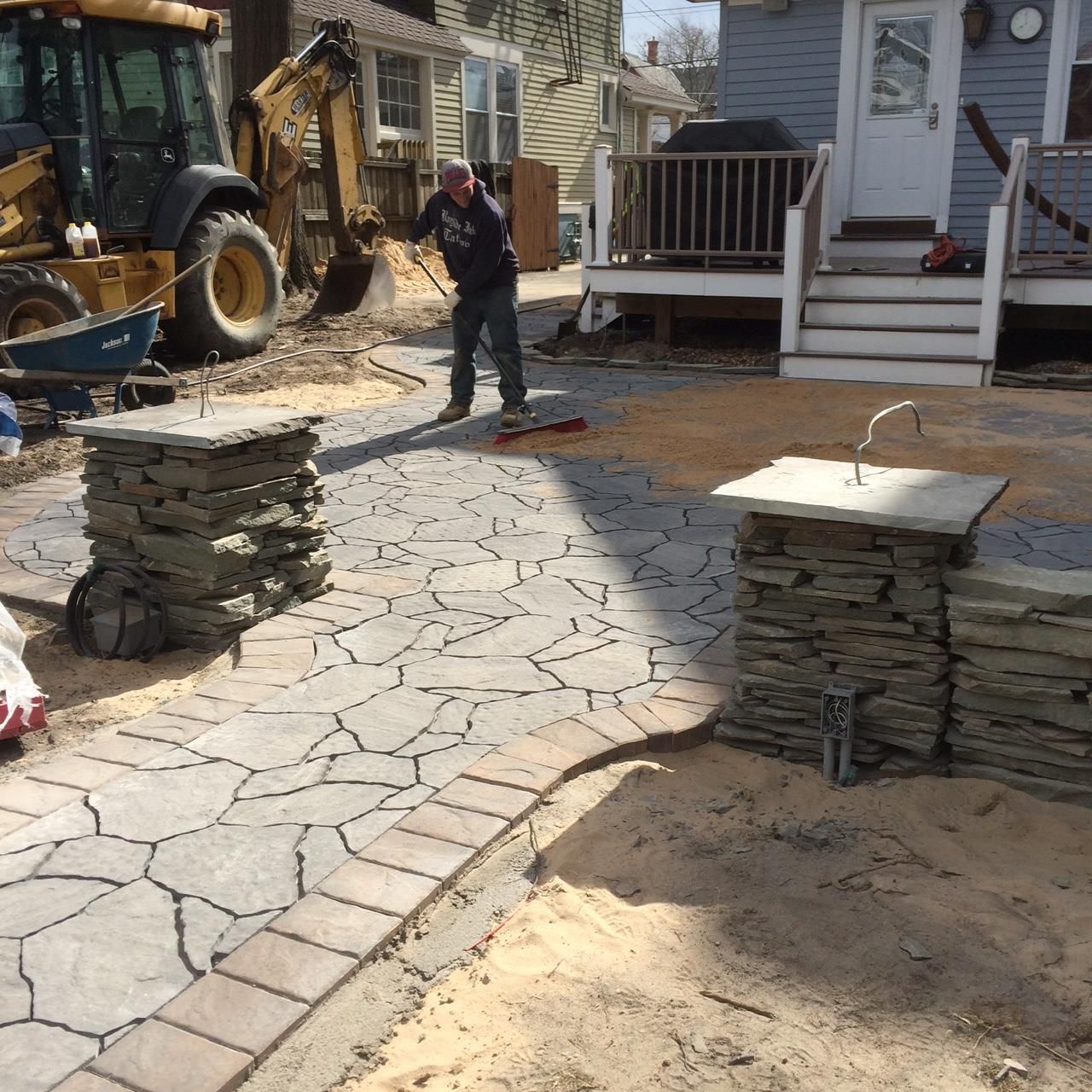 Masonry Contractor local to Rumson NJ. Worker installing stone pavers on a backyard walkway beside a house and tractor