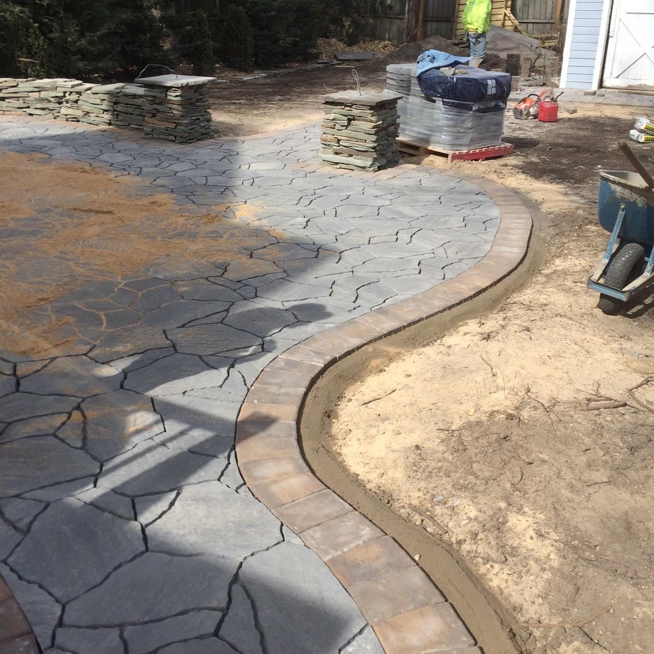 Curved stone paver walkway in Marlboro NJunder construction beside bare ground and stacked materials.