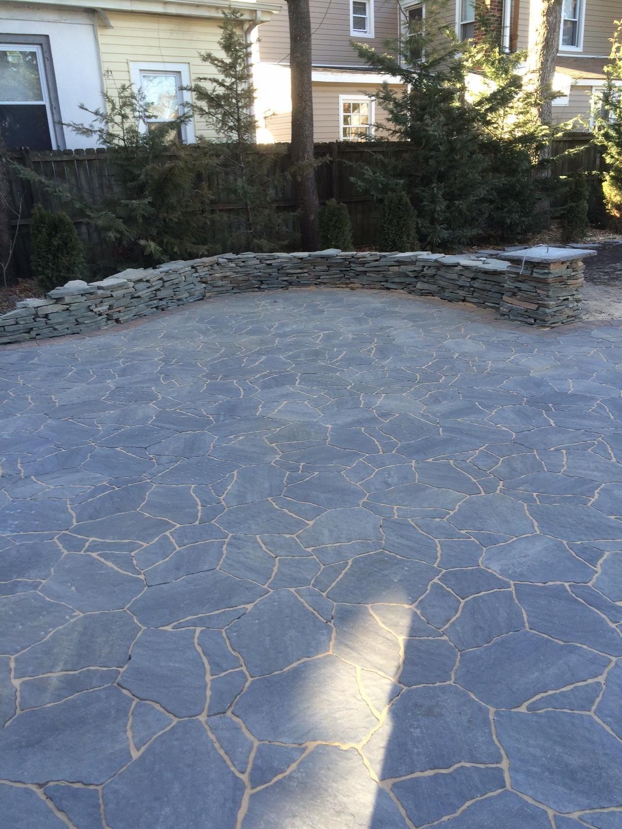 Stone-paved patio in Morganville NJ a backyard with a low stone wall and house in the background