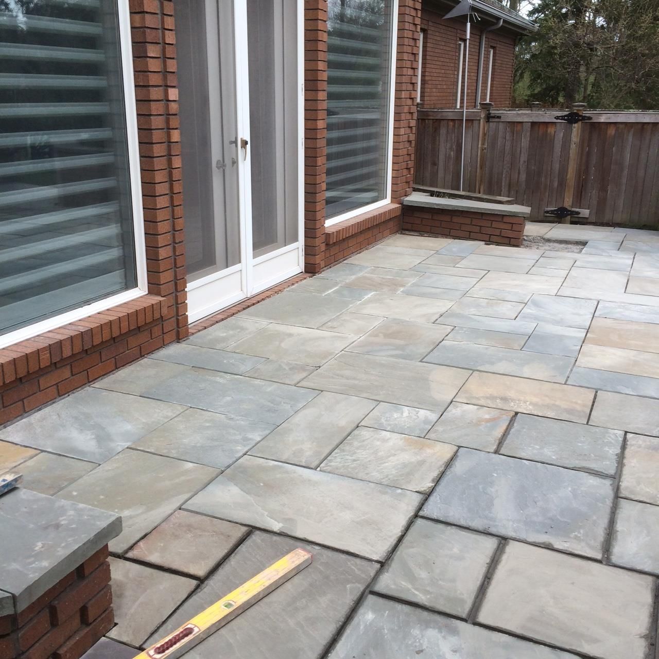 Masonry Contractor in Manalapan NJ. Patio with large gray paving stones beside a brick house and sliding glass doors