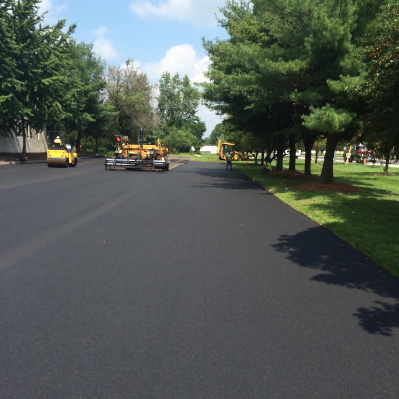 Private road paving in Colts Neck NJ, Freshly paved road with construction vehicles and workers along a tree-lined street