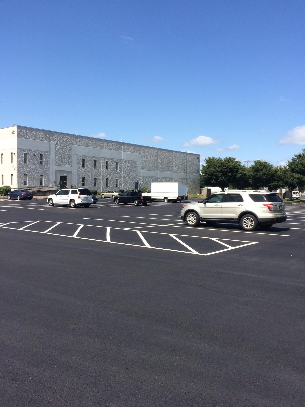 White building beside an empty parking lot with several parked cars under a clear blue sky.