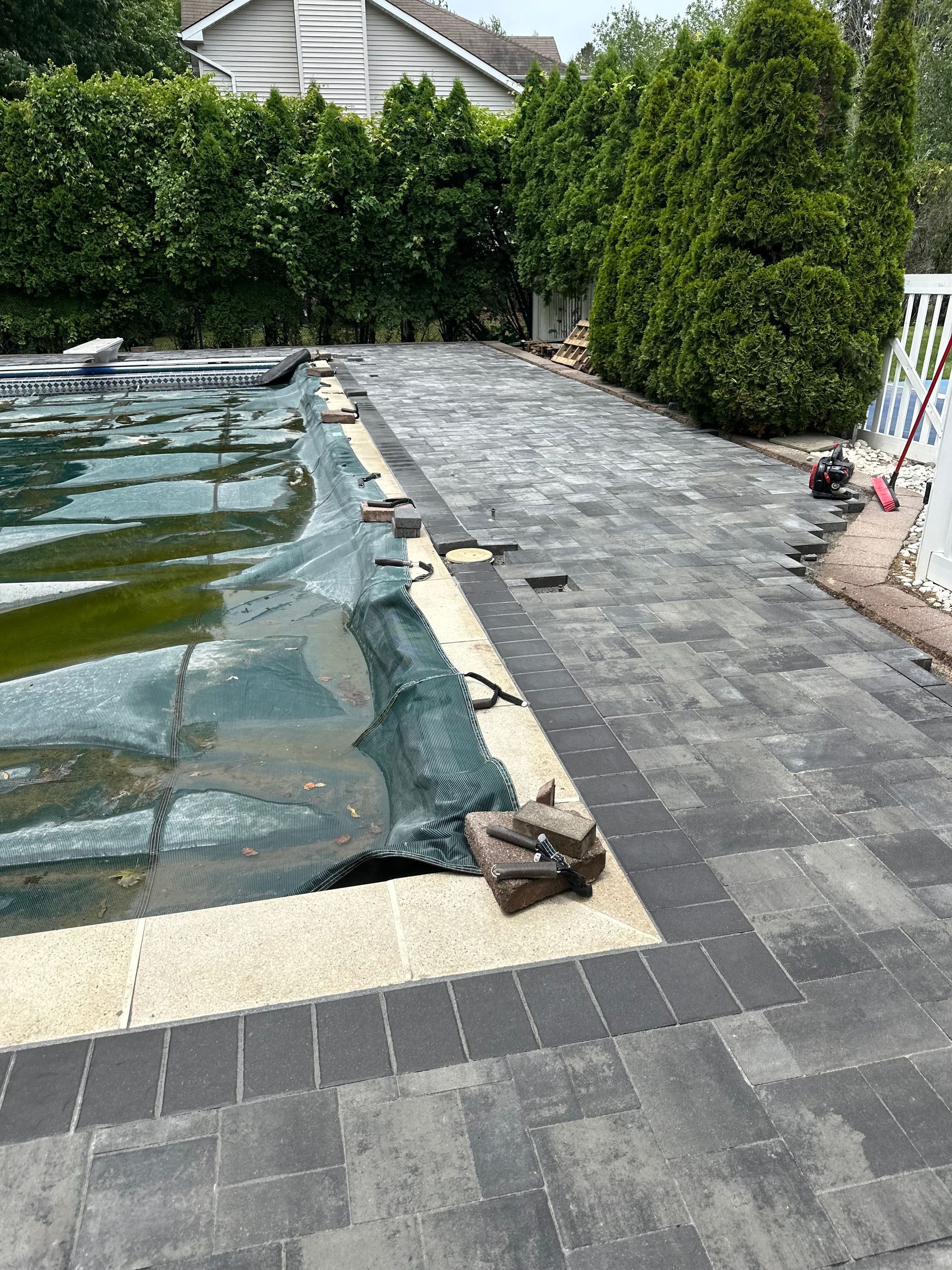 Local Brick Paver Company Holmdel NJCovered swimming pool beside a stone patio and tall green hedge in a backyard