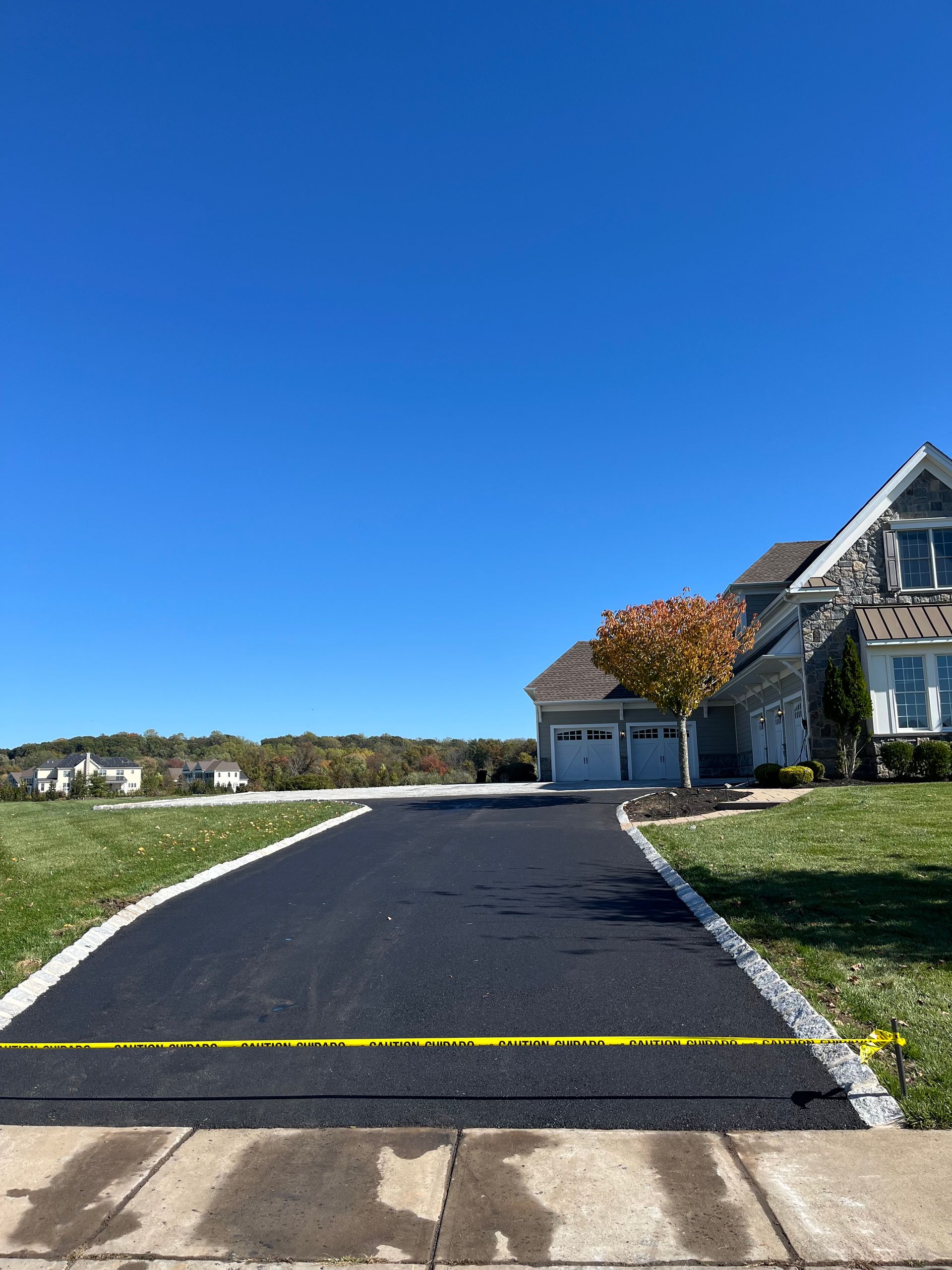 Colts Neck local paving company. Long driveway leading to a house with a garage under a clear blue sky.