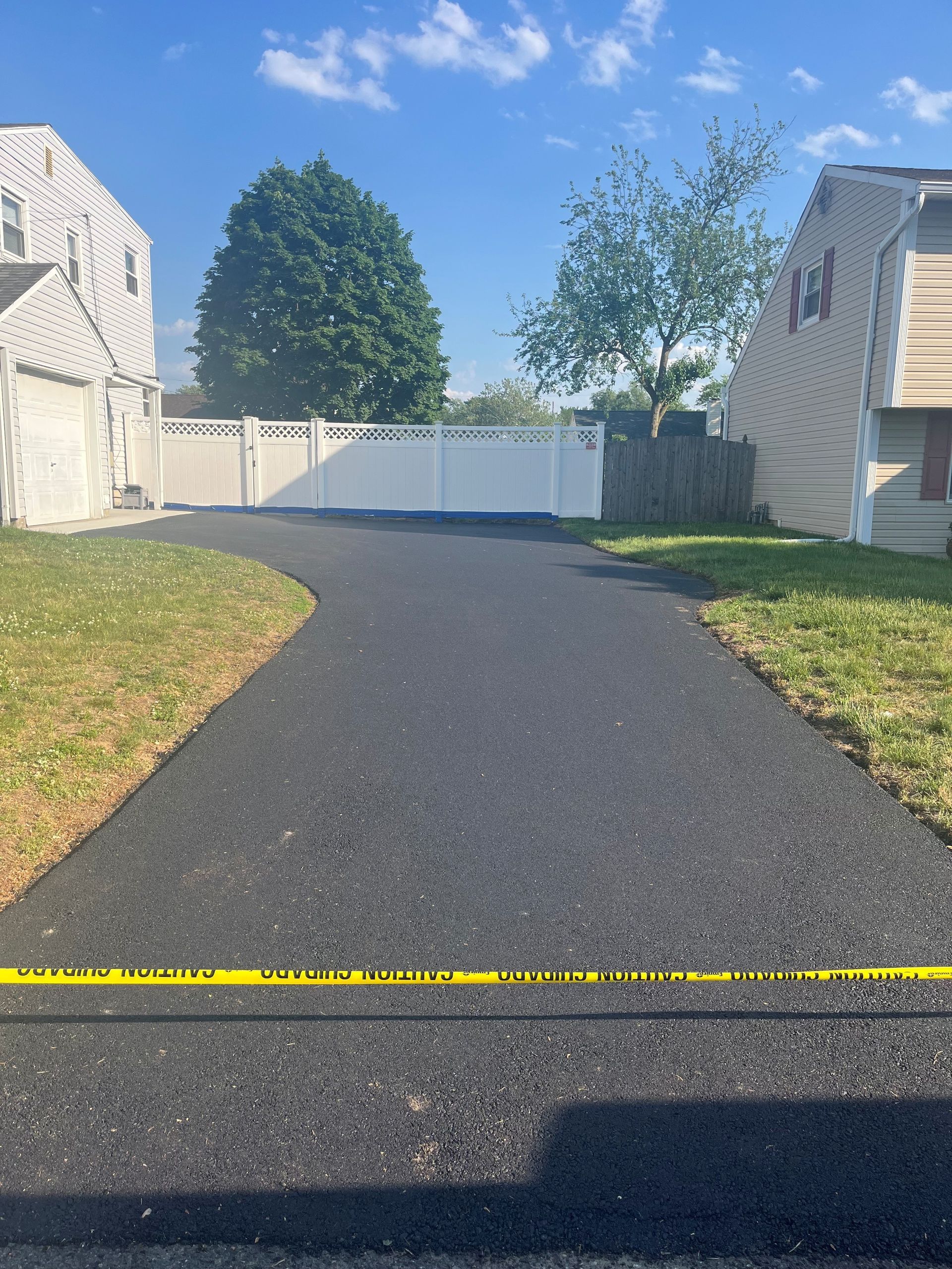 Looking for a paving contractor in Freehold? Curved driveway between townhouses leading to a white gate, with trees.