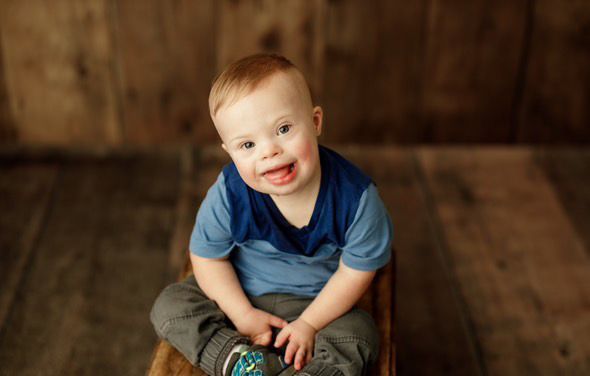 Boy with Down syndrome sitting, smiling at the camera.