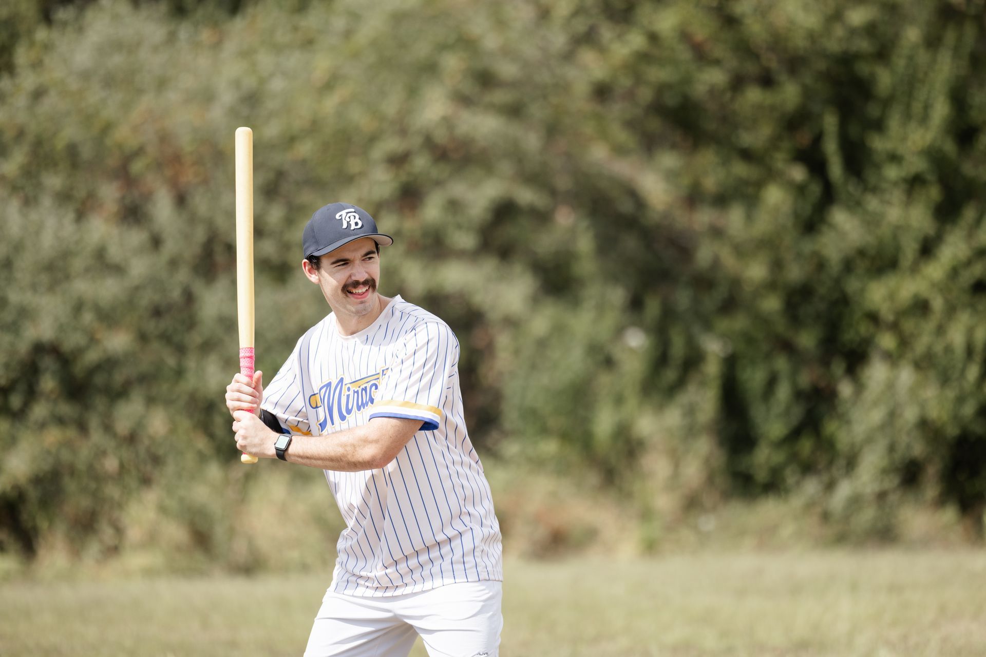 Man in wiffleball uniform, holding a bat, preparing to swing at a wiffleball on a field.