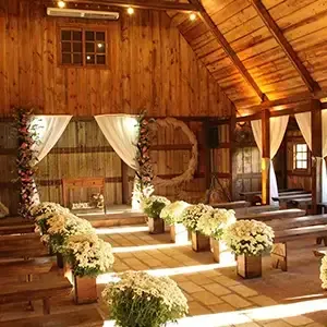 Rustic barn wedding aisle with white floral arrangements and draped curtains in warm sunlight