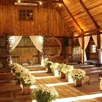 Rustic barn wedding aisle with white floral arrangements and draped curtains in warm sunlight