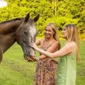 Two women petting a gray horse in a green field