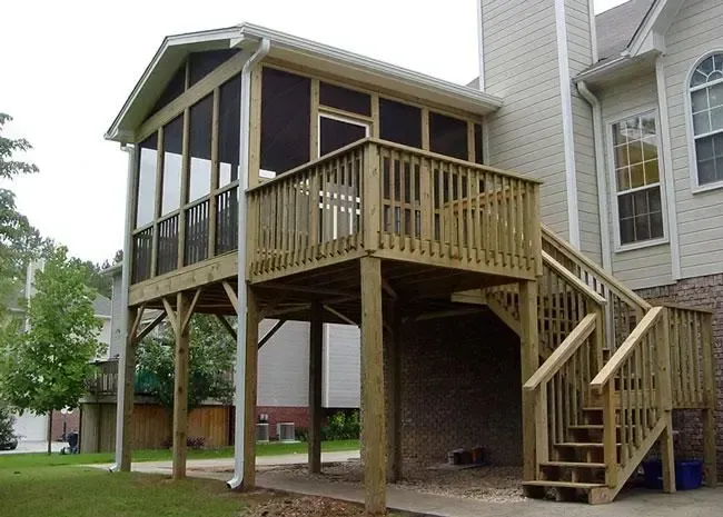 Elevated wooden deck and screened porch attached to the rear of a two-story beige house with stairs leading to the ground.