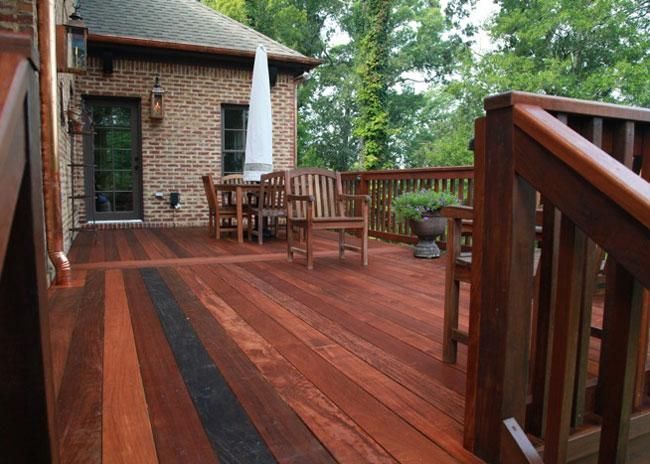A wooden deck with a dining set and stairs, attached to a brick house with a door and hanging lanterns.