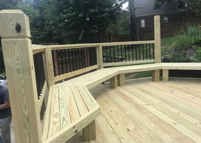 A wooden deck with built-in bench seating along a curved railing, featuring black metal balusters and a grassy background.