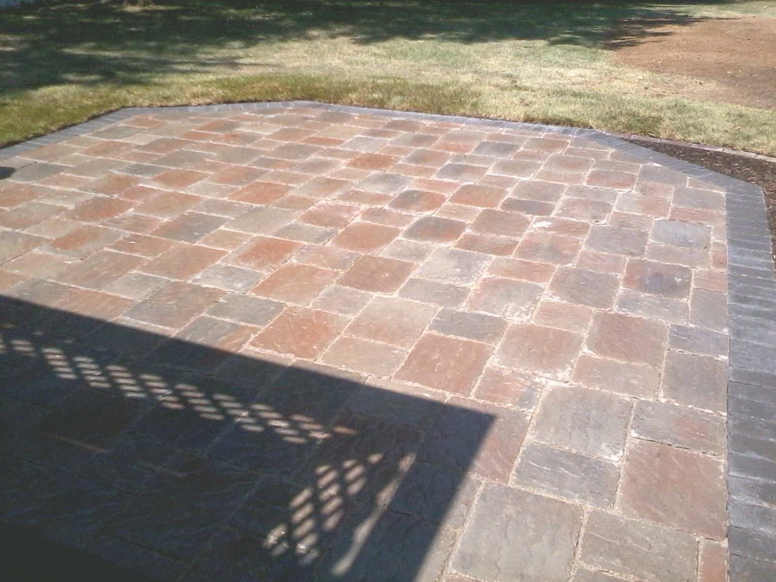 Paver stone patio in a yard with a shadow cast across the foreground.