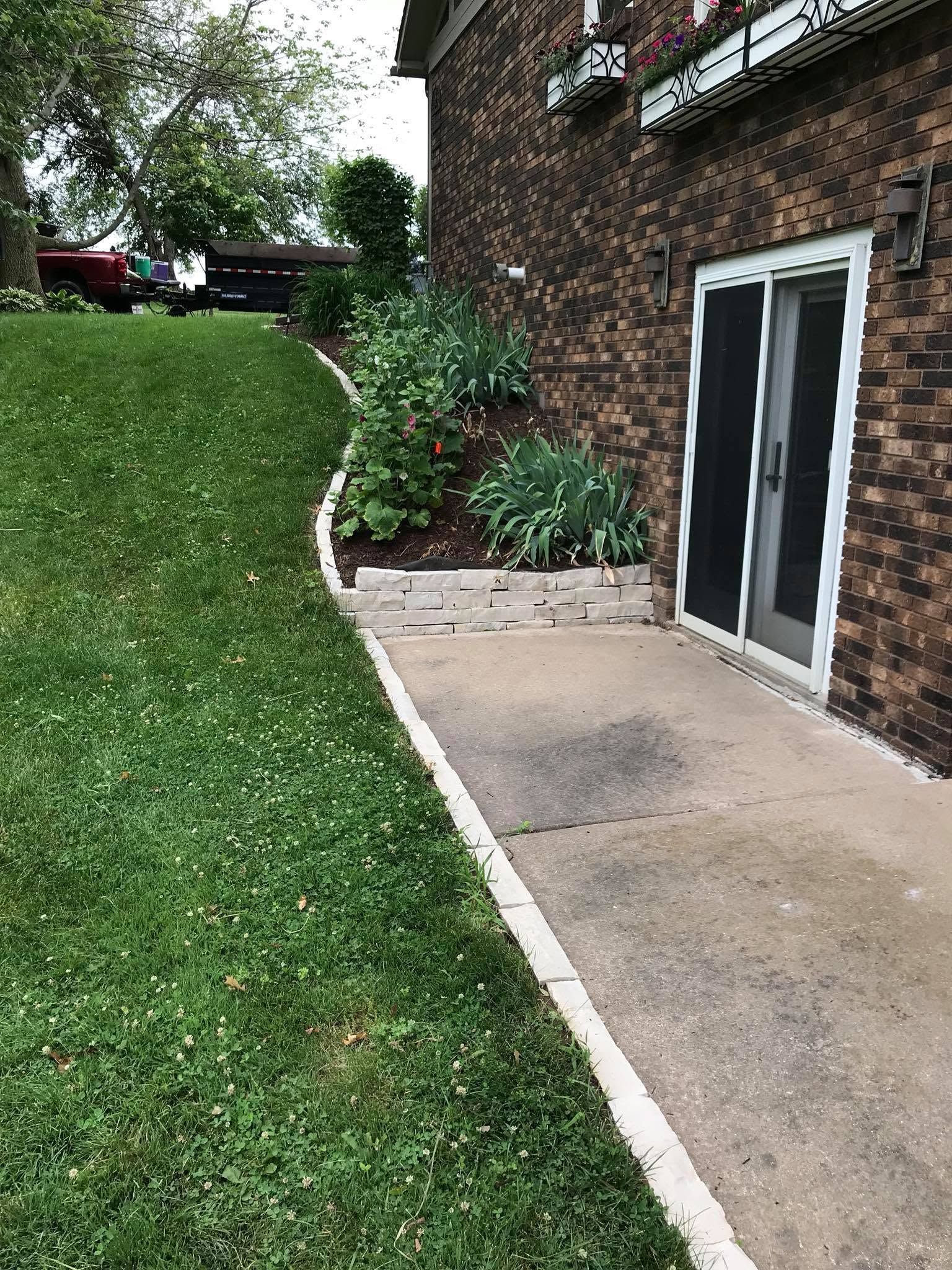 Brick house patio beside a grassy slope, with sliding glass doors and small garden beds.