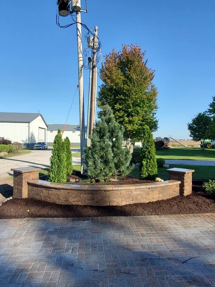 Landscaped roundabout with evergreen shrubs and a utility pole, beside a paved driveway on a sunny day