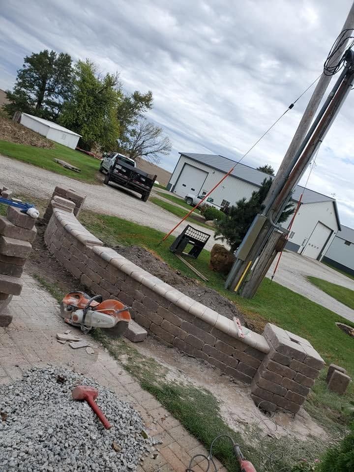 Construction site with gravel, a concrete wall, utility poles, and a pickup truck near white buildings.