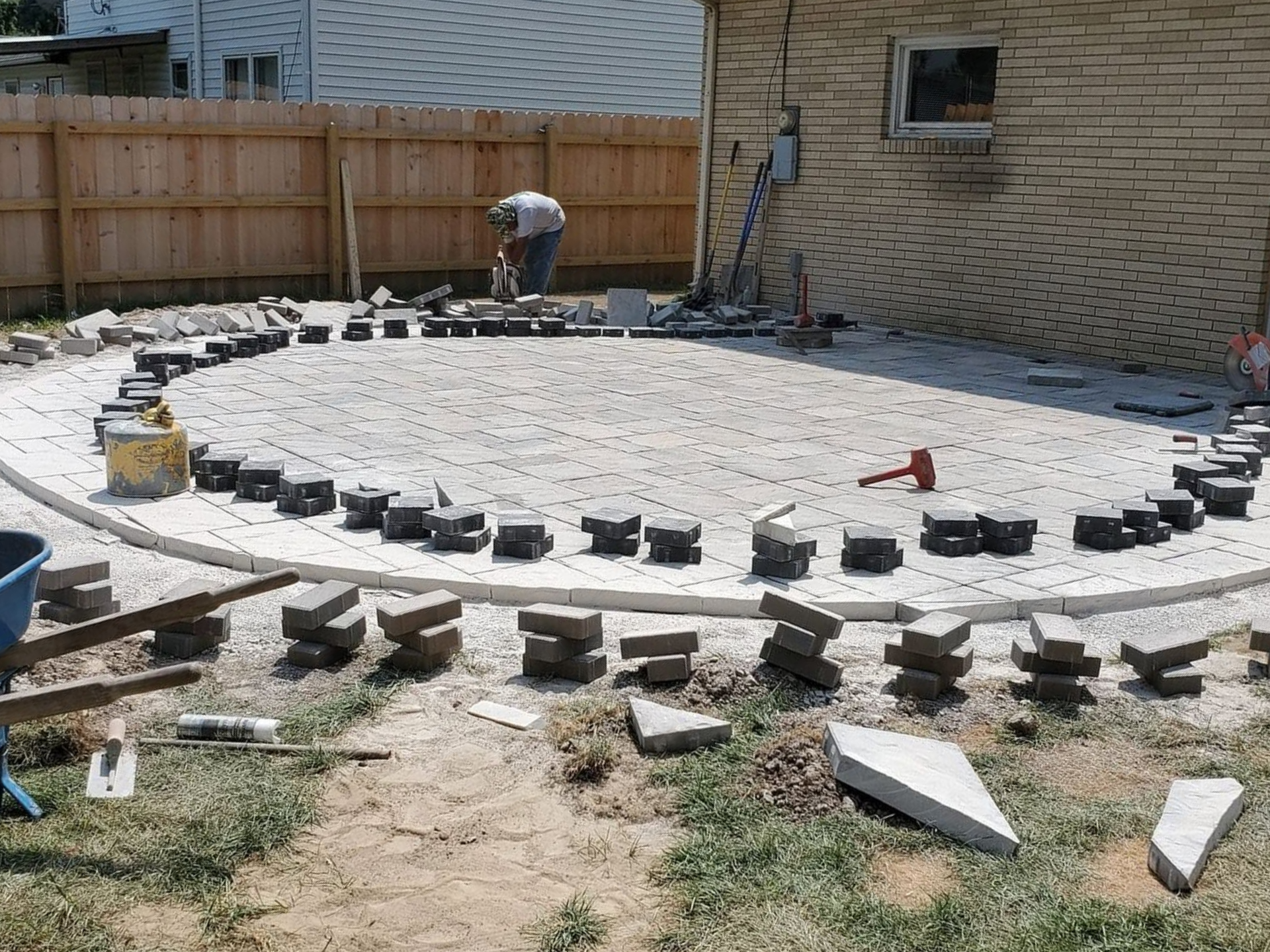 Backyard patio under construction with white gravel, stone border, and brick house wall