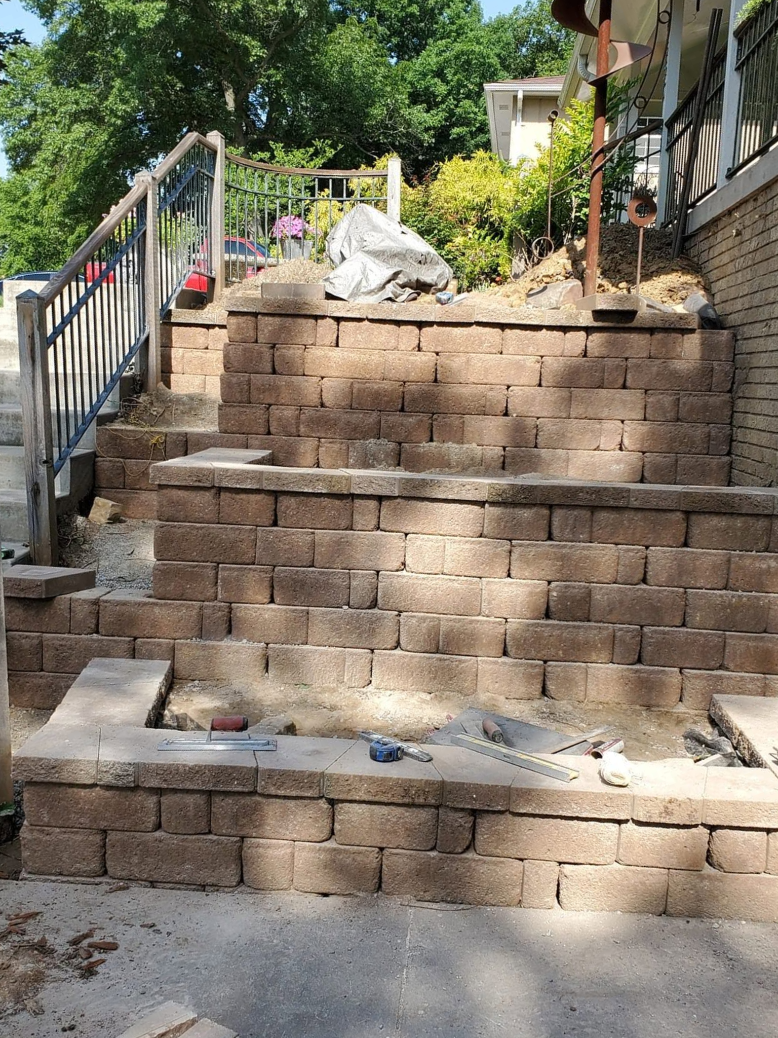 Steep outdoor staircase of wooden retaining walls and metal railings on a sunny hillside path