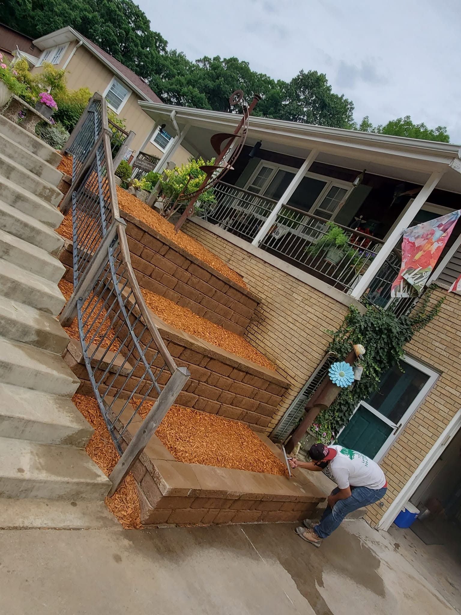 Worker shoveling mulch beside a house with terraced flower beds and stairs