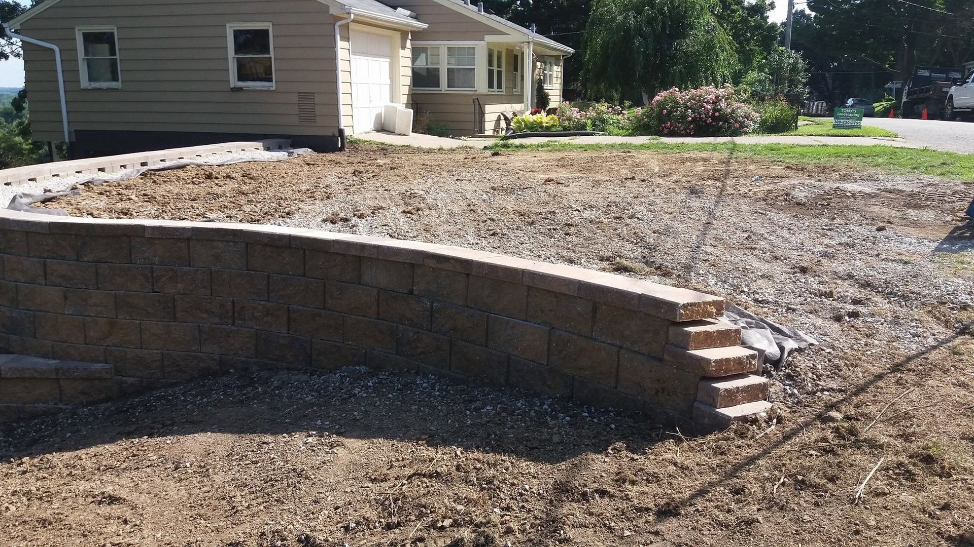 Curved stone retaining wall in a yard beside a house, with gravel and a grassy slope