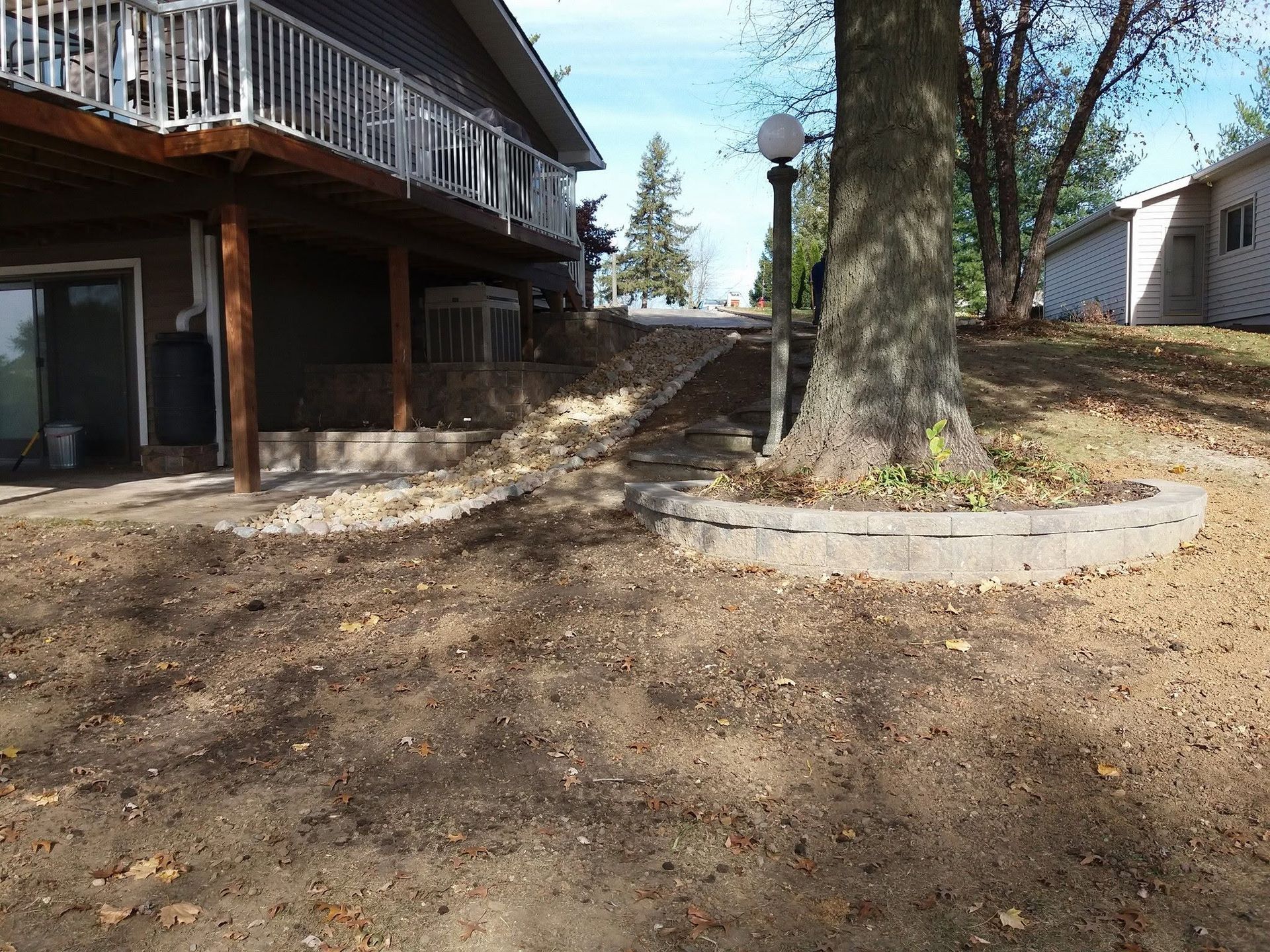 Backyard with a house deck, dirt ground, trees, and a circular stone planter