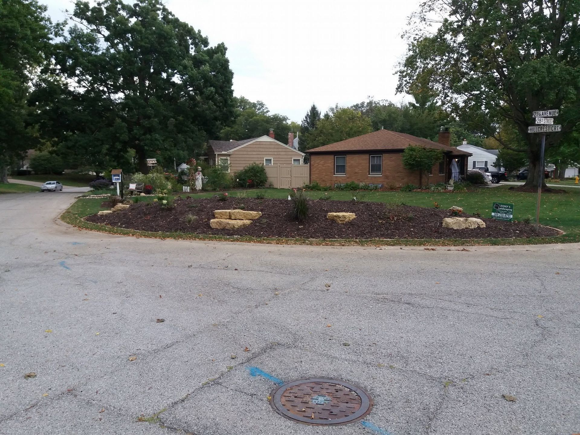 Small brick houses beyond a circular mulch bed on a quiet residential street under trees