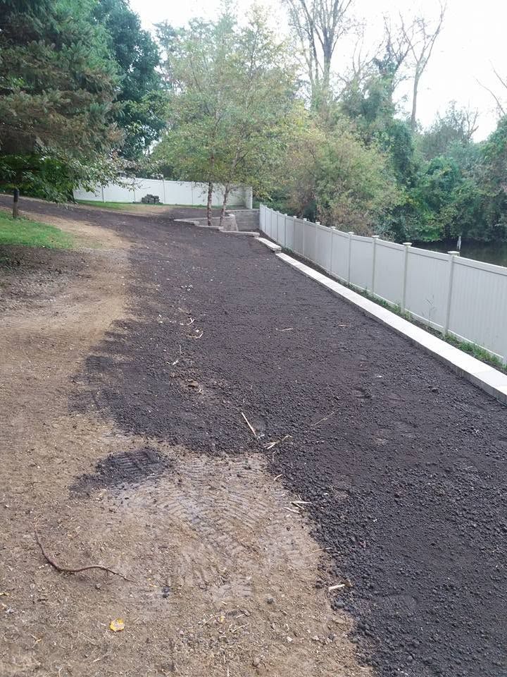 Dirt path beside a white fence, with trees and shrubs along a sloped yard.