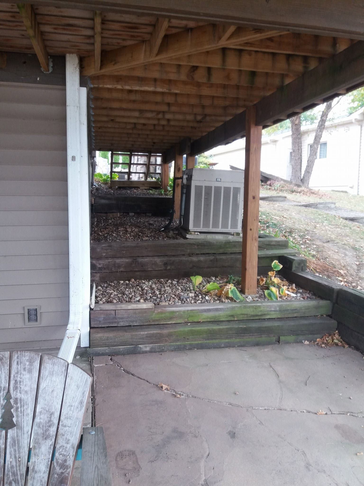 Covered outdoor walkway with wooden posts, steps, and an air conditioning unit beside a house