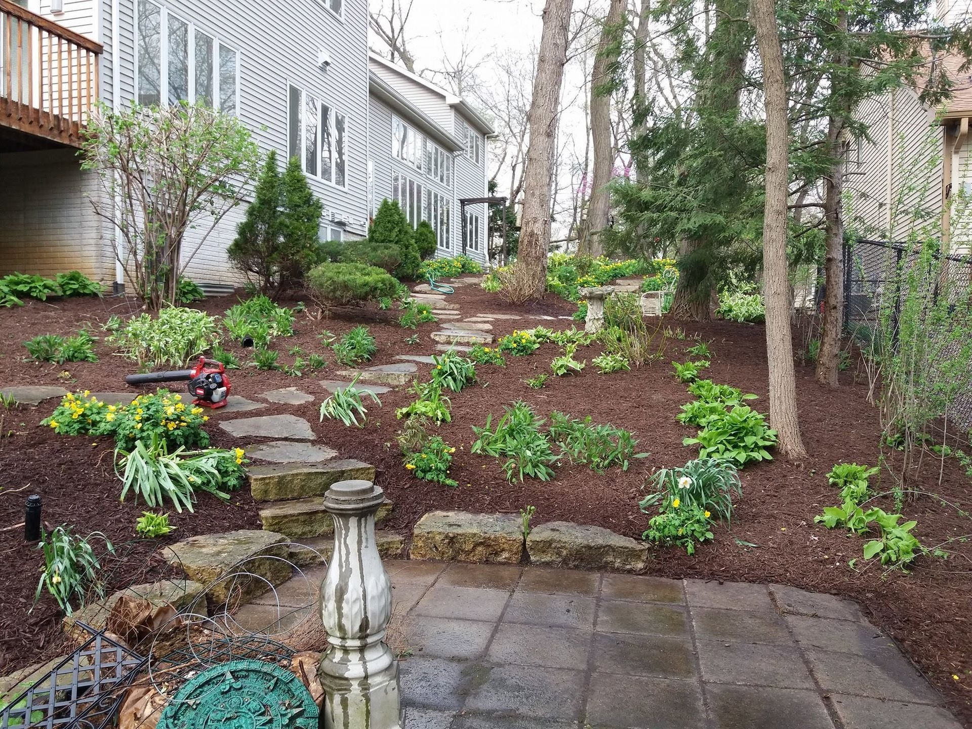 Stone patio overlooking a sloped garden with young shrubs, trees, and a house on either side