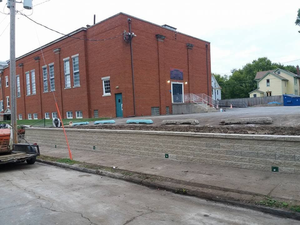 Brick industrial building on a street corner beside a low concrete wall and construction debris.