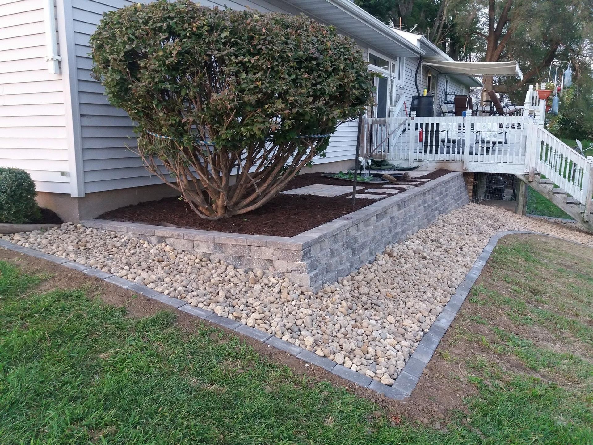 Landscaped front yard with stone retaining wall, gravel beds, and trimmed shrub beside a house porch