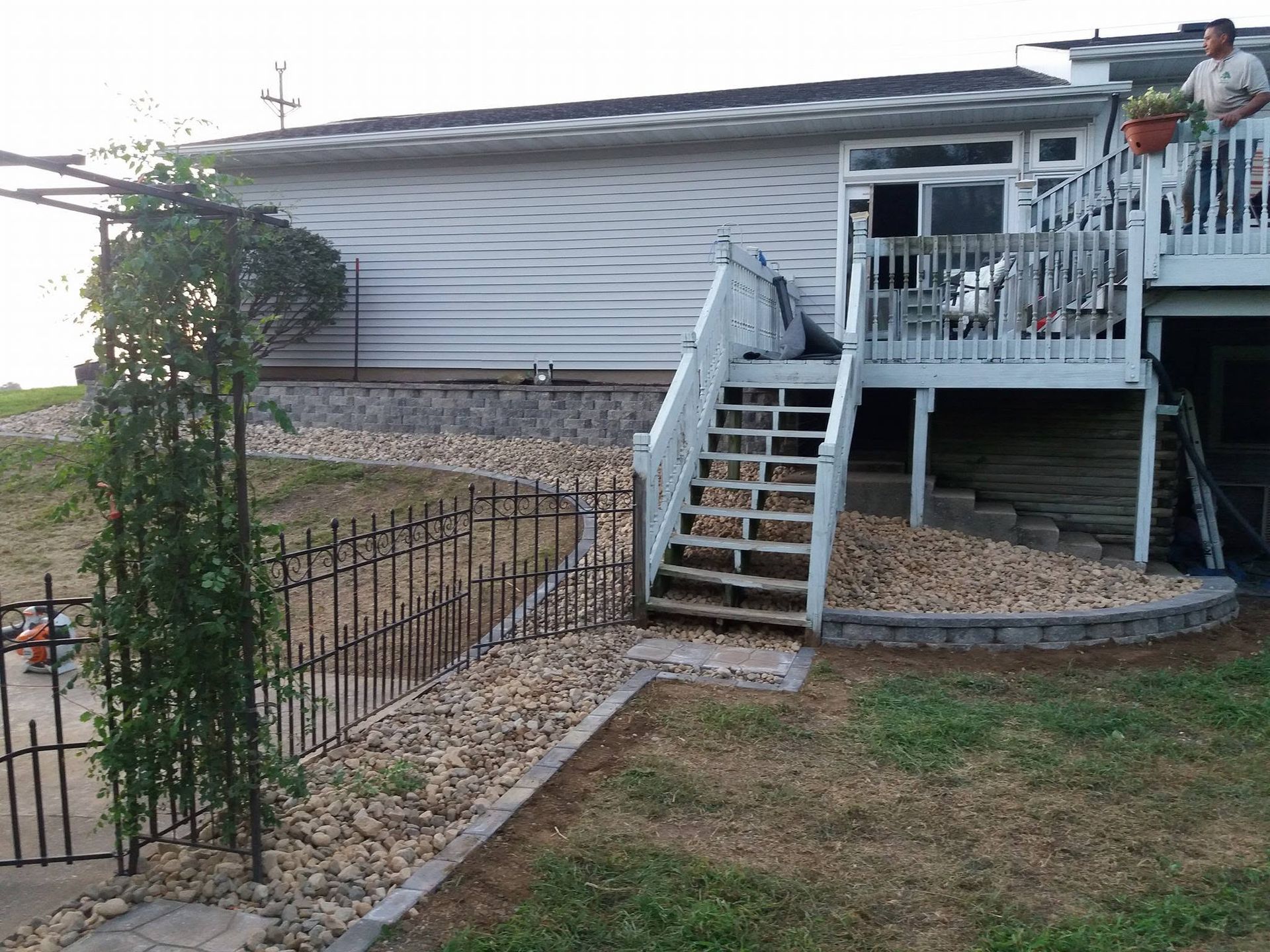 Backyard deck with stairs, white railing, and stone retaining wall beside a house