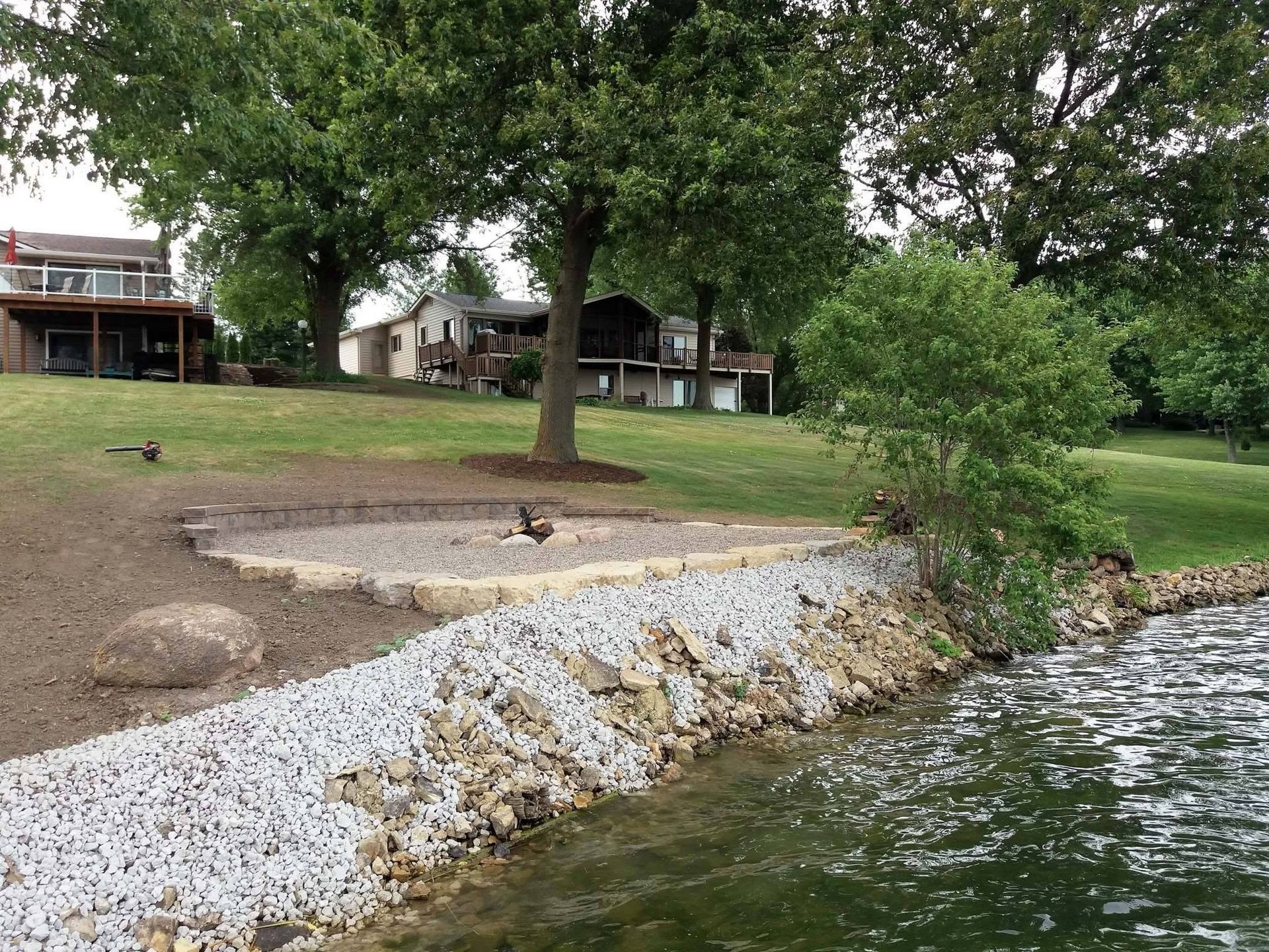 Rocky lakeshore with trees, a grassy bank, and houses in the background