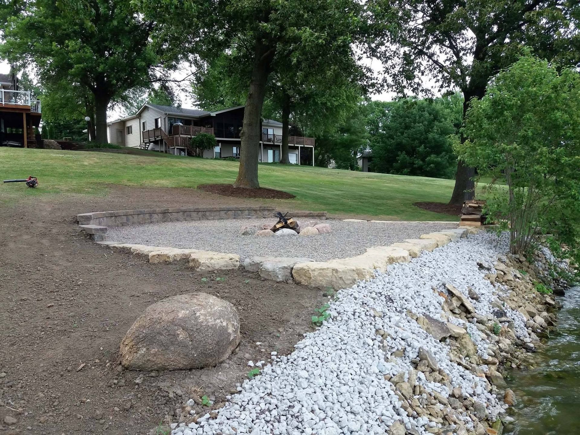 A dirt yard with rocks, a gravel border, trees, and a house in the background.