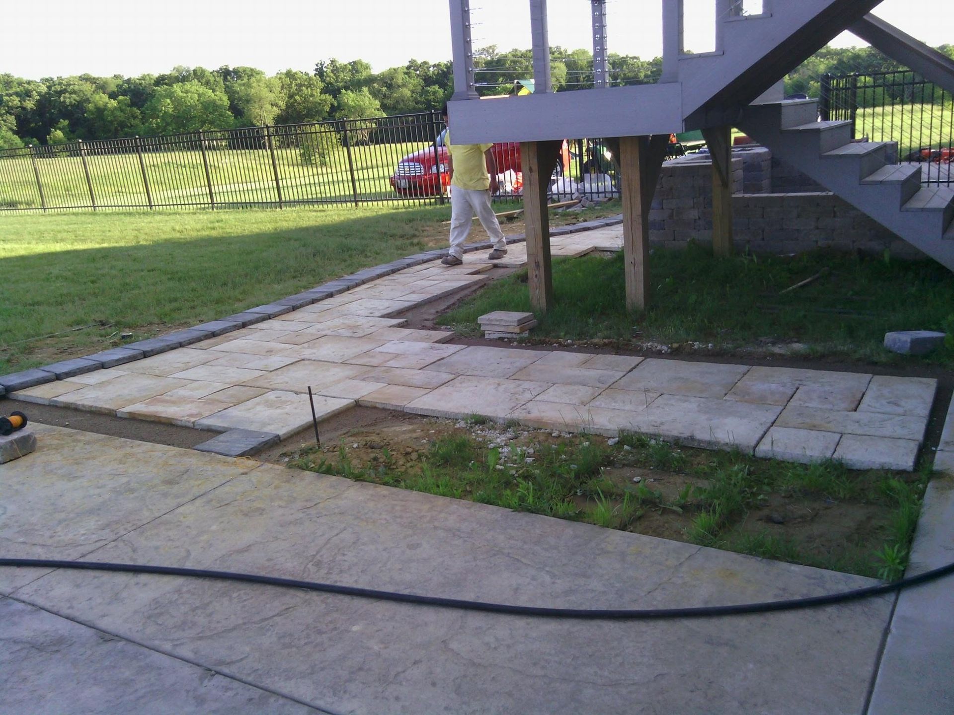 Backyard patio with concrete walkway, stairs, grass, and a hose lying across the ground