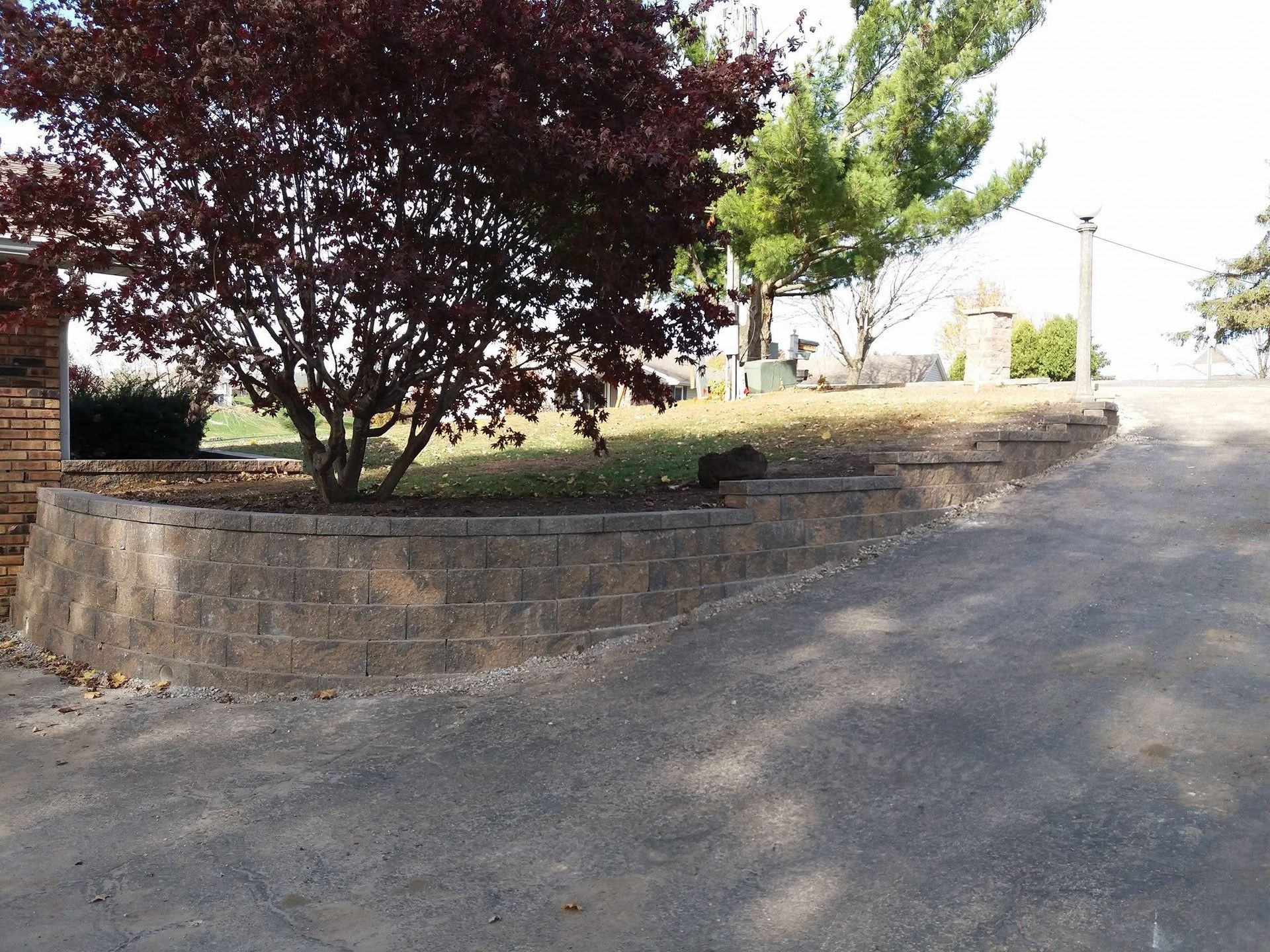 Stone retaining wall beside a gravel path with trees and a bright open area beyond