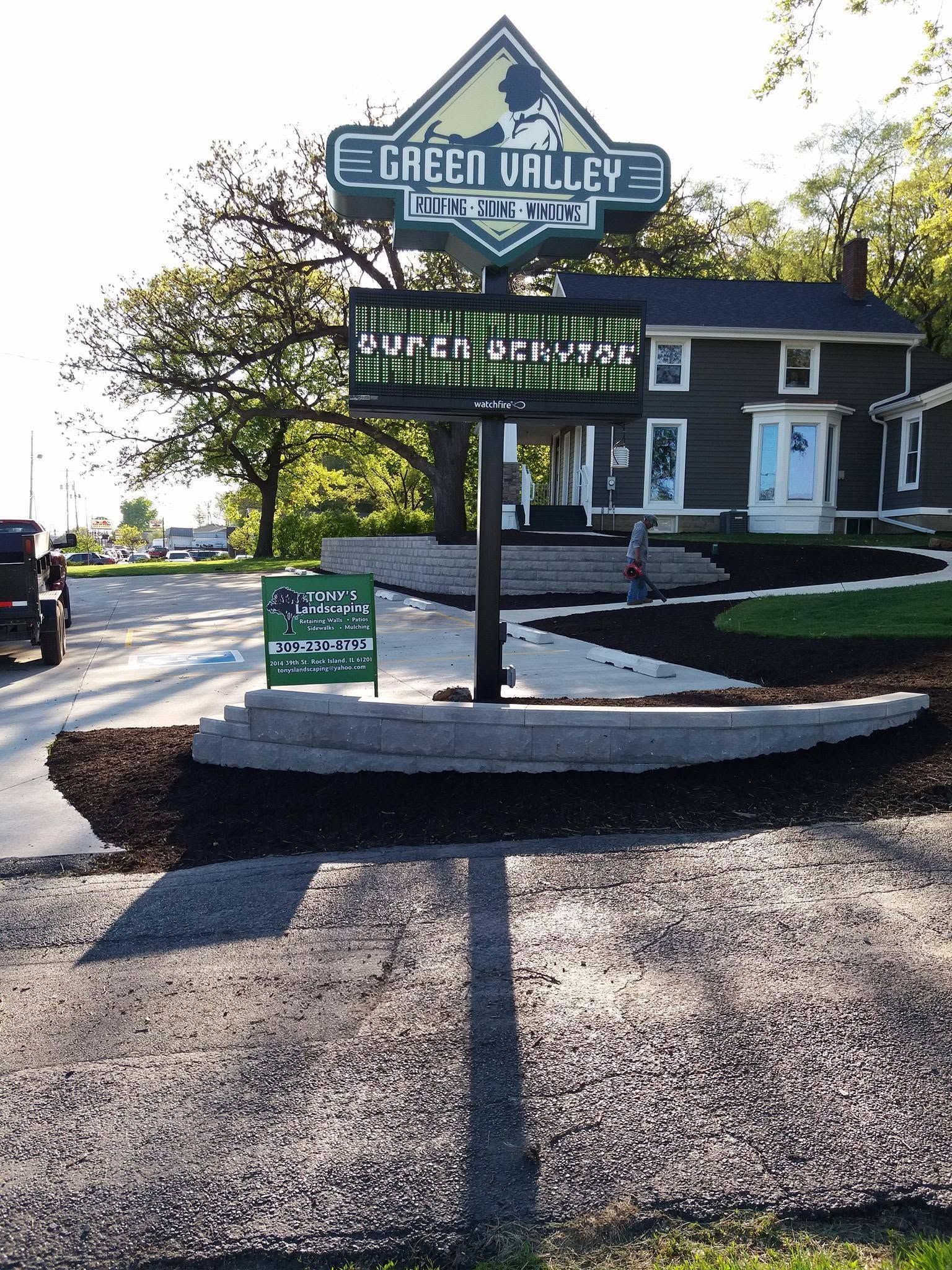 Green Valley sign at a roadside entrance beside a small office building on a sunny day