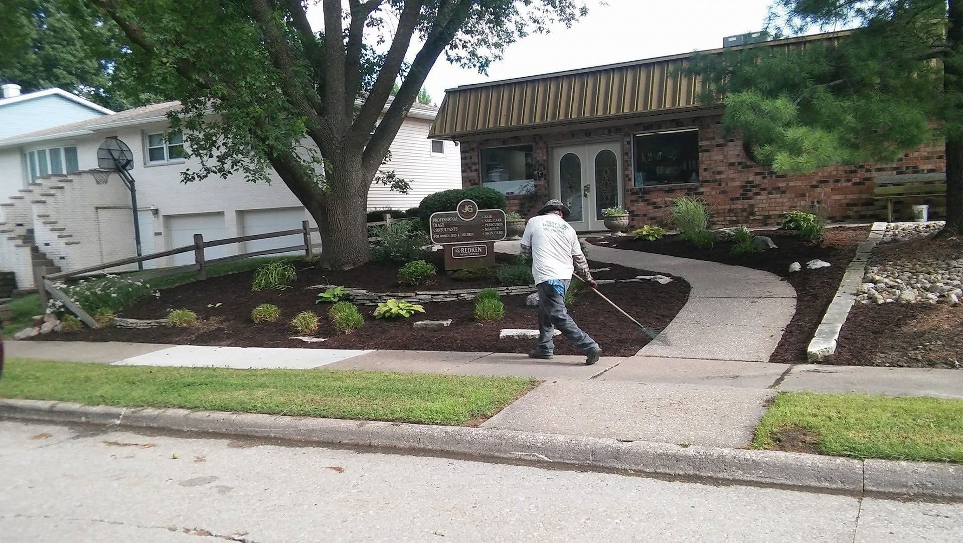 Person walking on a curved path beside a landscaped front yard and house after rain