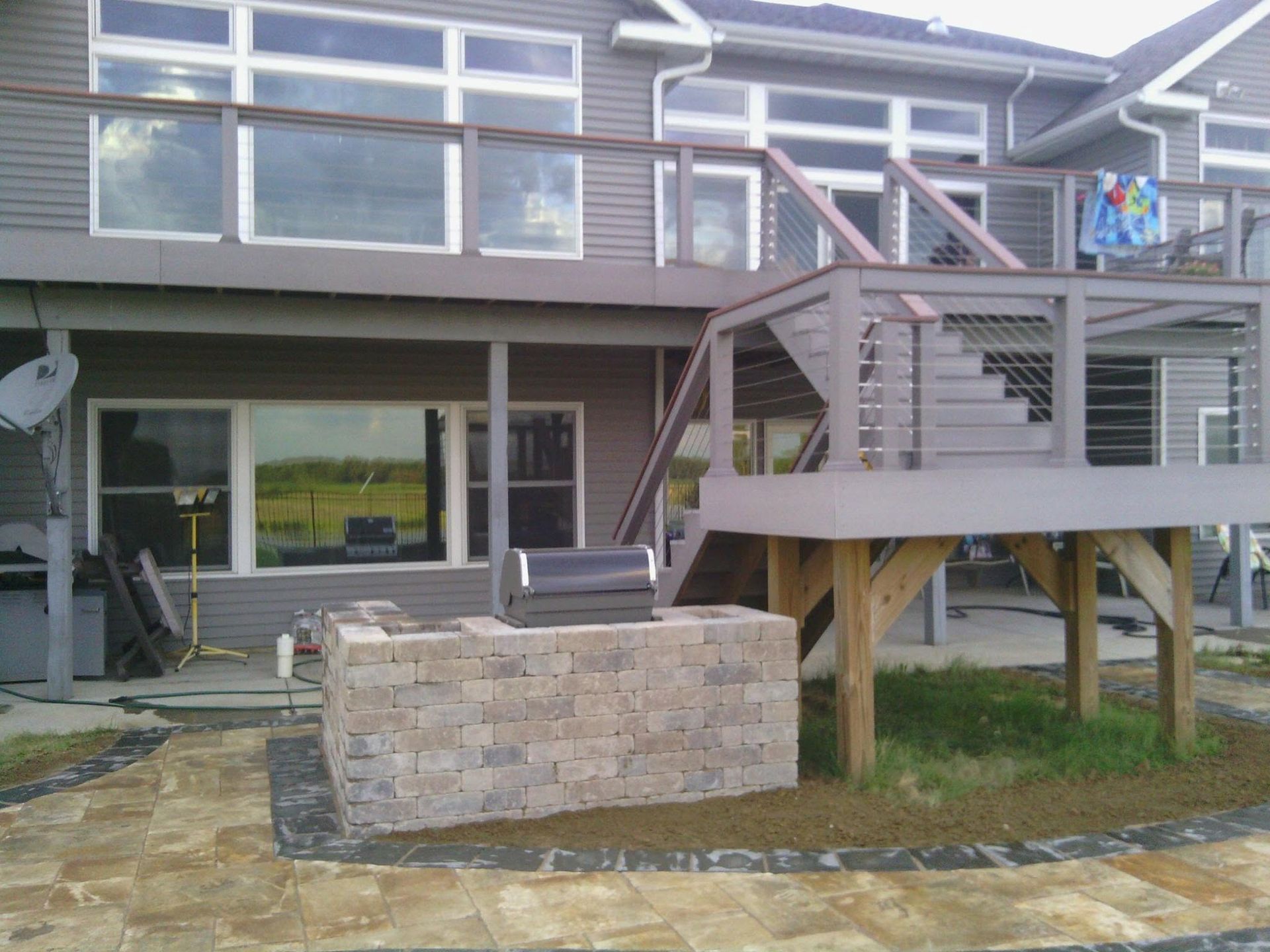 Backyard deck with stairs, glass railing, and a hot tub beside a stone patio and stone fire pit.