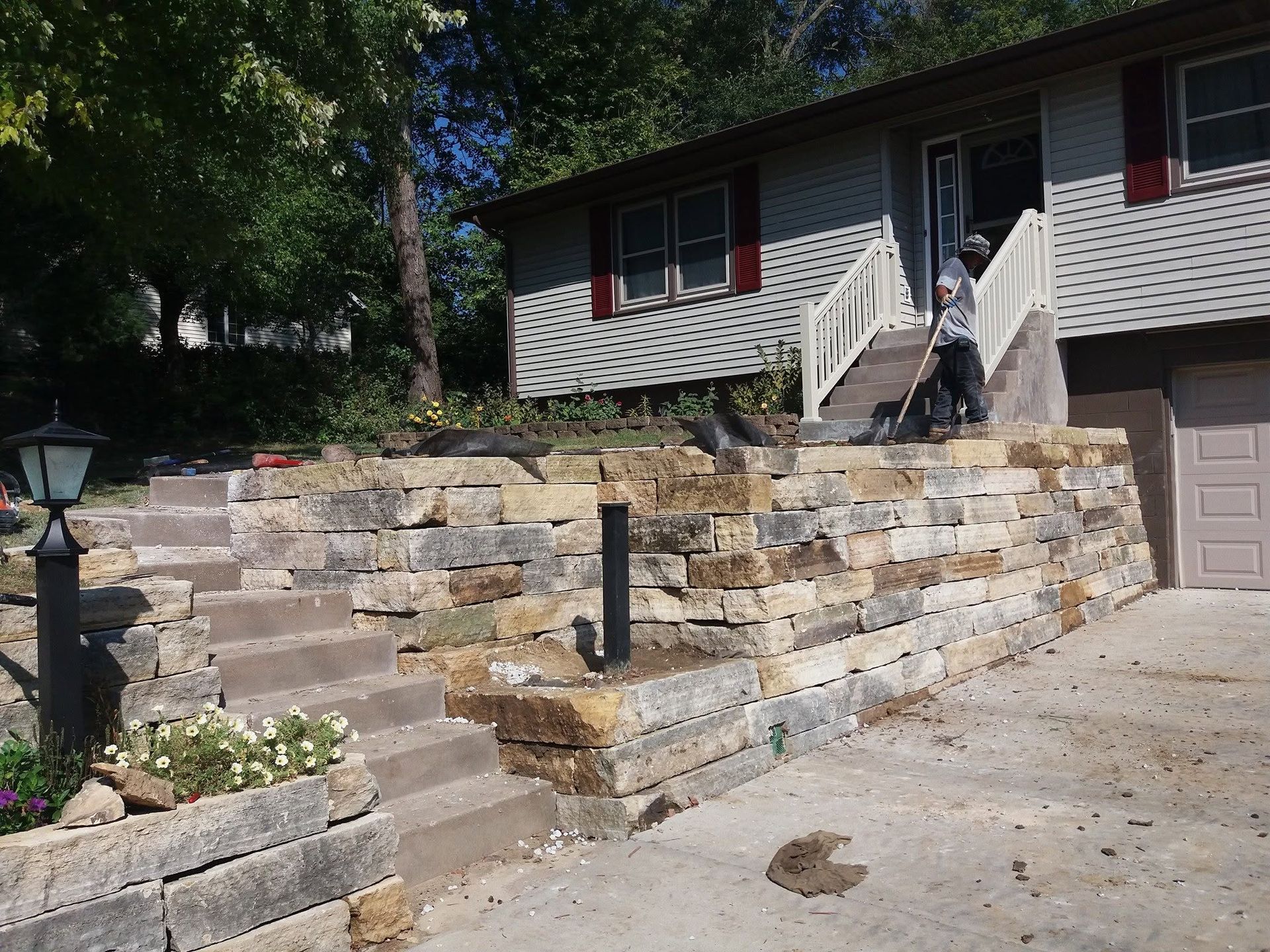 Stone retaining wall and front steps leading to a house with a person standing on the porch.