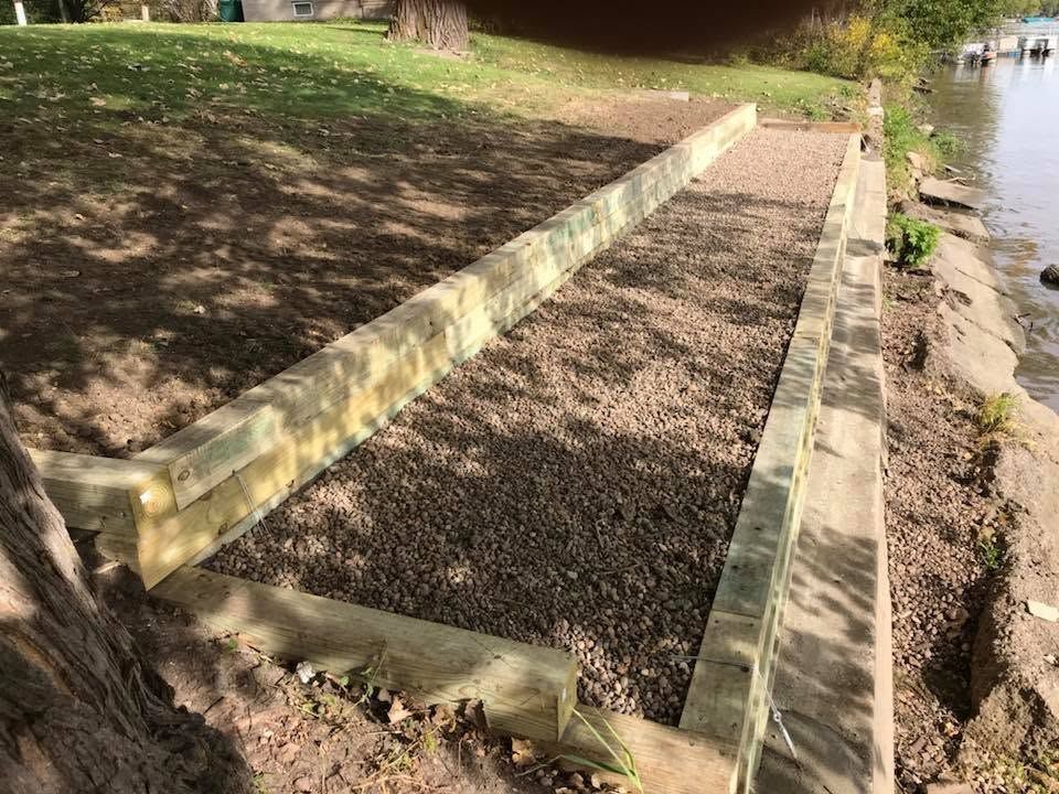 Stone-edged gravel drainage channel beside a riverbank in a park area
