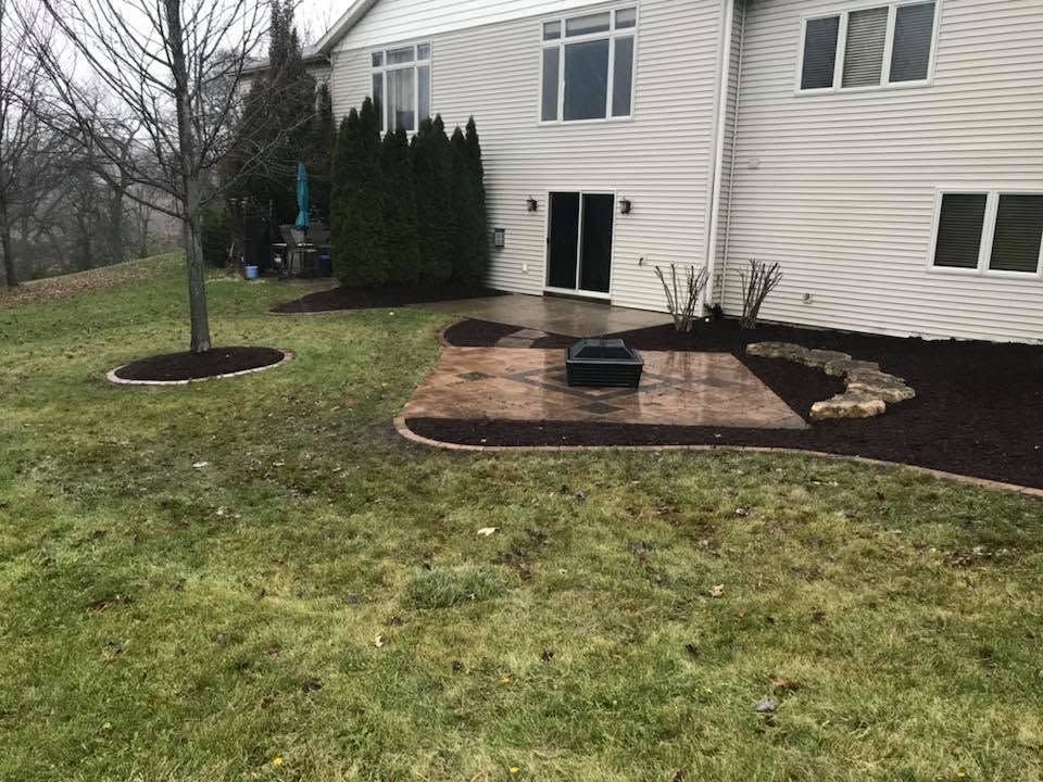 Backyard patio with brick pavers, black planter, and a beige house with sliding doors.