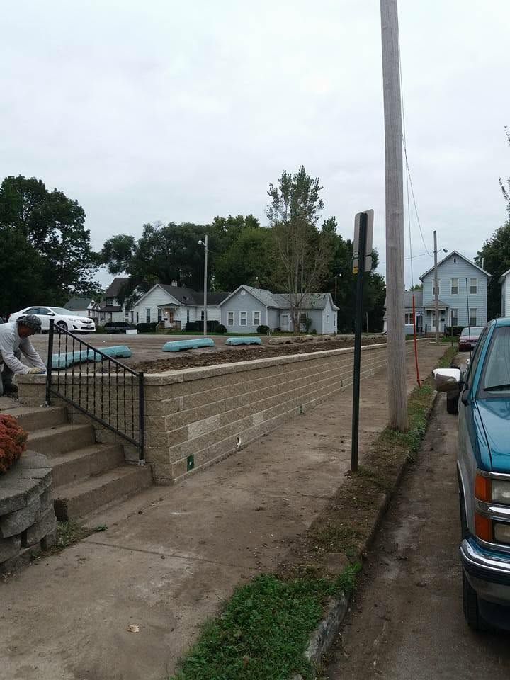 Construction site with a brick retaining wall, utility pole, and houses in the background