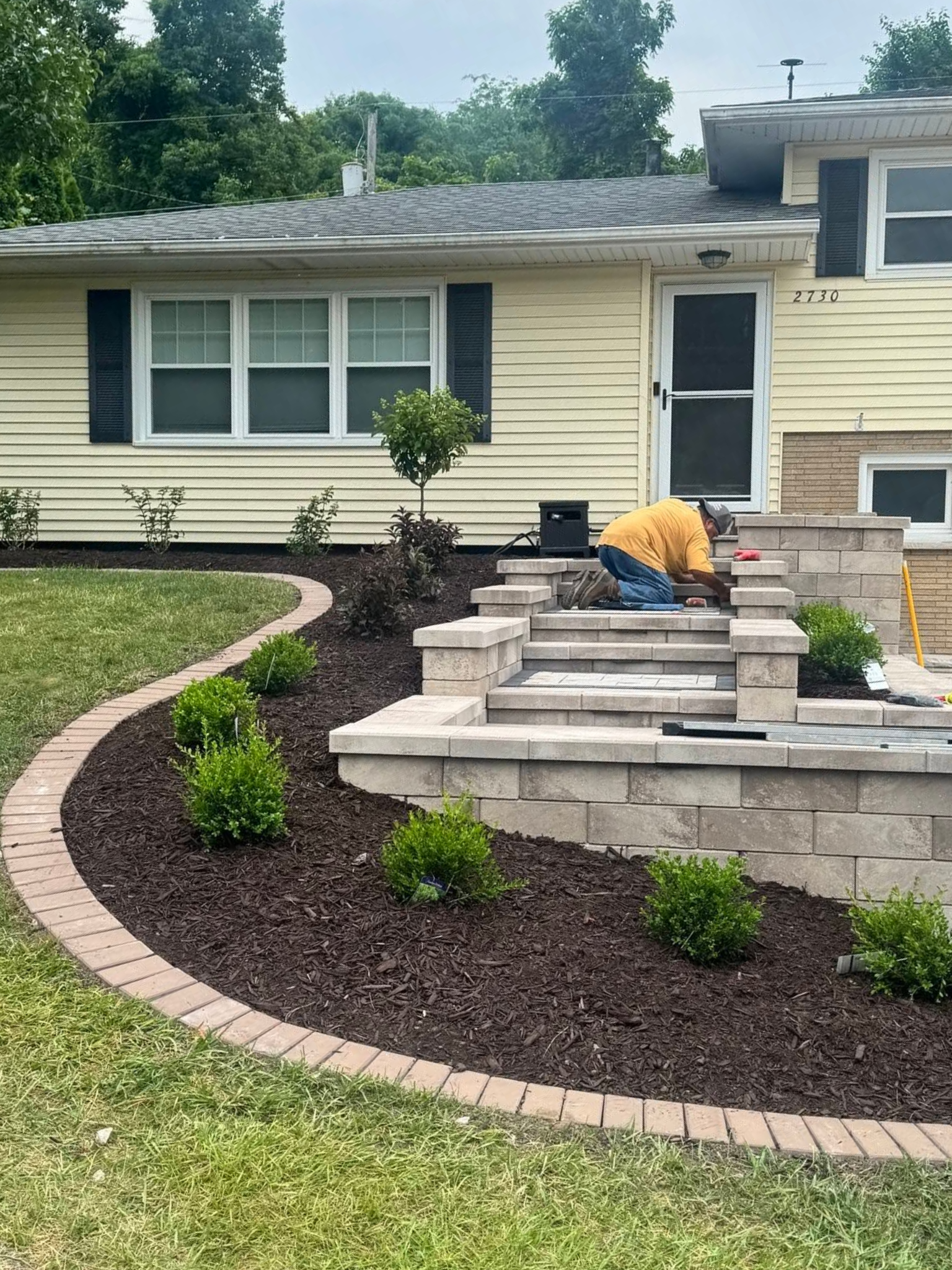 Suburban house with landscaped front yard, curved mulch bed, and stone steps leading to the porch